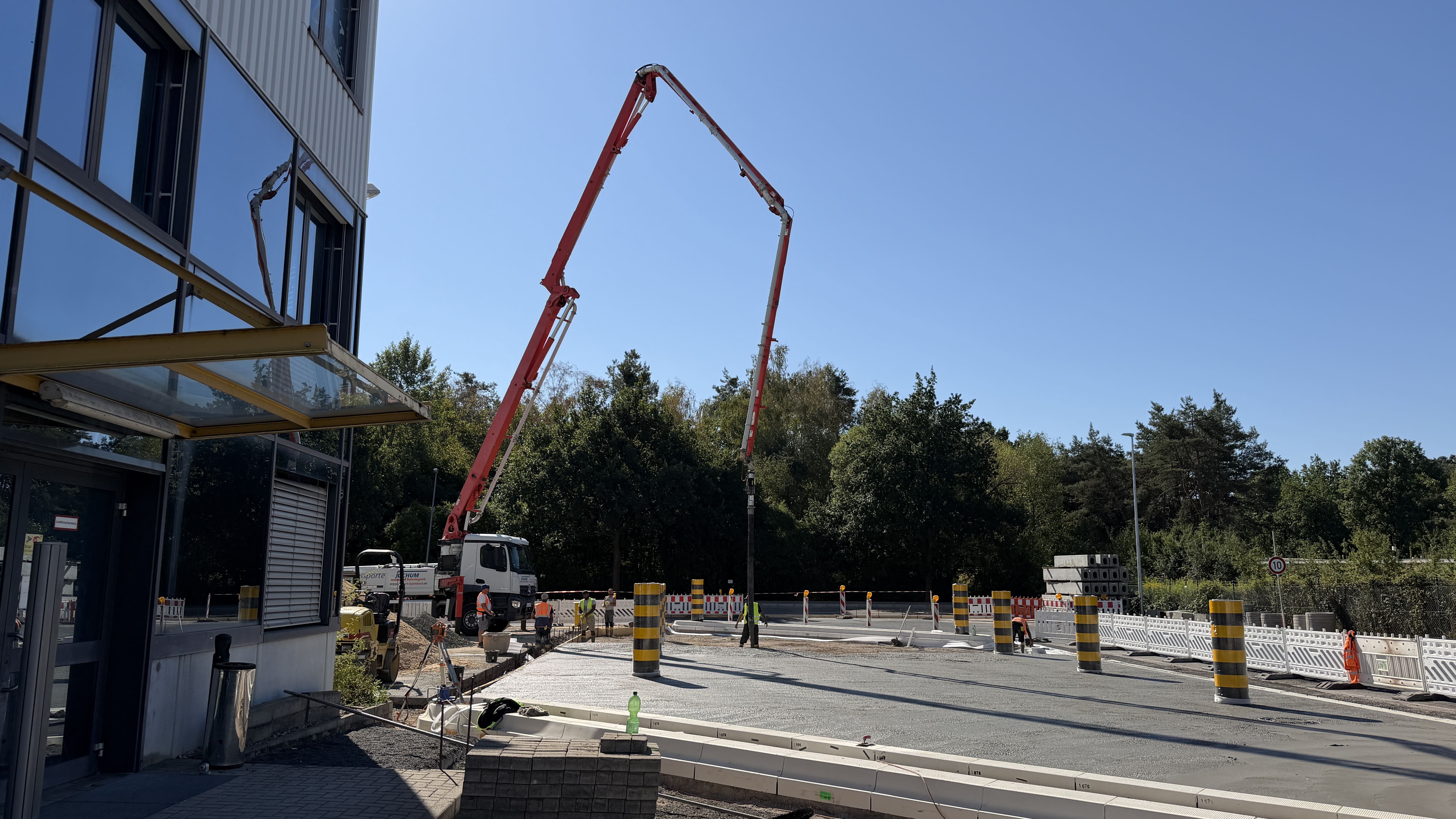 Große Autobetonpumpe beim Gießen der Betonfläche vor einem Industriegebäude.